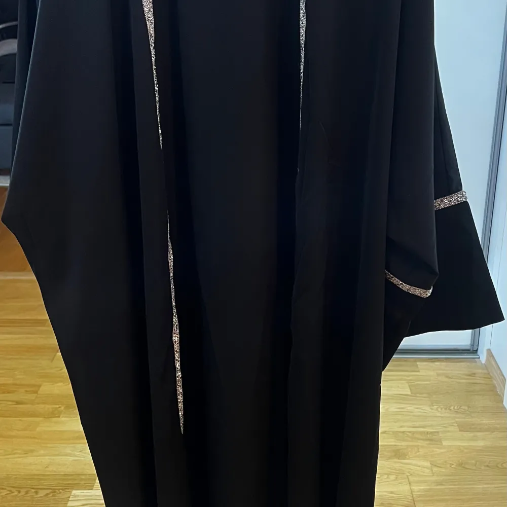 En svart öppen abaya med silver stenar, paljetter och glitter detaljer längs med kanterna och armarna. Den är en helt ny produkt med prislappen på. Helt o använd och den är i storlek S. Men den funkar absolut till större storlekar också då den är lit. Mekot.