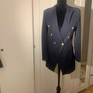 Mörkblå kavaj med guldknappar - Säljer en elegant mörkblå kavaj med snygga guldknappar. Den har en klassisk design med långärmad stil och en figursydd passform. Perfekt för både formella tillfällen och vardagsbruk. Passar bra till höst och vår. Medföljande byxor. 