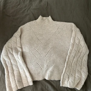 Vit stickad tröja med kabelmönster - Säljer en supermysig vit stickad tröja med ett snyggt lmönster på ärmarna. Den är i nyskick, utan prislapp. Storlek M.