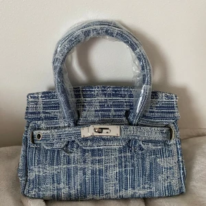 Denim väska - Säljer denna söta lilla väska i denim då den tyvärr inte kommer till användning. Långt axelremsband och coola accessoarer medföljer.  Väskan är i nyskick, aldrig använd. 