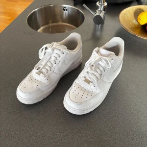 Vita Nike Air Force sneakers - Säljer ett par klassiska vita Nike Air Force sneakers. De är i väldigt bra skick med lite smuts på sulorna, som kan tvättas bort enkelt. Perfekta för vardagsbruk och passar till nästan alla outfits. Storlek 42. Nypris: 1395 kr.
