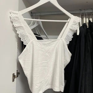 Vit topp med spetsdetaljer från H&M - Säljer en superfin vit topp från H&M i storlek S, passar M. Den har vackra spetsdetaljer på axelbanden som ger en romantisk touch. Perfekt för sommardagar eller en avslappnad fest. Toppen är oanvänd och redo för nya äventyr!