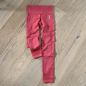 Rosa leggings från Gymshark - Säljer ett par snygga rosa träningstights från Gymshark. De är högmidjade och har en tight passform, perfekt för träning. Materialet är stretchigt och bekvämt, med snygga ribbade detaljer längs sidorna. Perfekta för gymmet eller yoga!