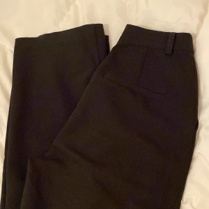 Svarta kostymbyxor från Claire Rose - Snygga svarta kostymbyxor från Claire Rose med hög midja och dragkedja. Perfekta för en stilren look. Byxorna har en klassisk design med bälteshällor och diskreta fickor.