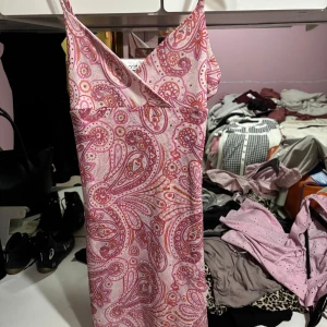 Rosa paisleymönstrad klänning från Currants - Snygg rosa klänning med paisleymönster från Currants. Klänningen har smala axelband och en v-ringad design. Perfekt för en somrig look!