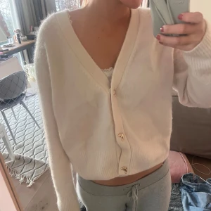 Vit kofta från & Other Stories - Mysig vit kofta från & Other Stories med v-ringning och knappar framtill. Perfekt för en avslappnad look. Koftan har långa ärmar och är tillverkad i ett mjukt material.