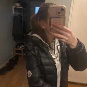 Svart dunjacka från Moncler - Snygg svart dunjacka från Moncler med dragkedja och hög krage. Knappen som man ska snäppa / dra upp är sönder men den går att stänga ändå där av priset dagkjedorna går inte heller att dra upp eller ner men har inte testa så mycket så de kan nog gå