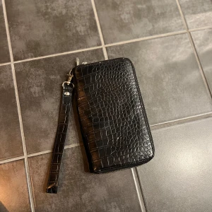 Svart plånbok  - Snygg svart plånbok med dragkedja. Den har flera fack inuti för kort och kontanter. Aldrig använd. Nyskick.