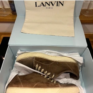 Bruna sneakers från Lanvin - Snygga bruna sneakers från Lanvin i mocka med snörning. Skorna har en stilren design med ljus sula och är perfekta för en avslappnad look.
