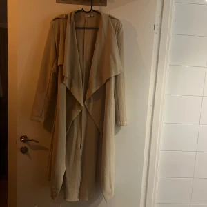 Beige trenchcoat  - Snygg beige trenchcoat från Object med knytband i midjan och långa ärmar. Säljer då den inte kommer till användning. Fint skick, använt få gånger. 