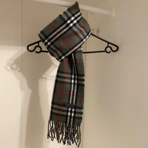 Burberry - Säljer nu denna Snygga halsduk från Burberry i färgen grå. Tillverkad i mjukt lammull med klassiskt fransad kant. Perfekt för att hålla dig varm och stilren under kyliga dagar. Hör av er vid funderingar☺️