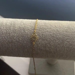 Guldarmband med solmotiv - Elegant guldarmband med ett solmotiv i mitten. Perfekt för att lägga till en touch av stil och elegans till din look. Kedjan är tunn och smidig, vilket gör den bekväm att bära hela dagen.