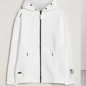 Vit hoodie från Ralph Lauren - Säljer en stilren vit hoodie från Ralph Lauren med dragkedja och huva. Den har tryckdetaljer på ärmen och praktiska fickor framtill. Perfekt för en avslappnad look. Ny pris: 3399kr