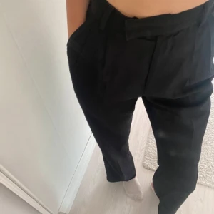 Svarta byxor från Stories - Snygga svarta byxor från Stories i storlek 36.  Byxorna har en elastisk midja och stängs med dragkedja och knapp. Perfekta för en stilren look. Se bilderna för måtten, innerbenslängden är 80cm