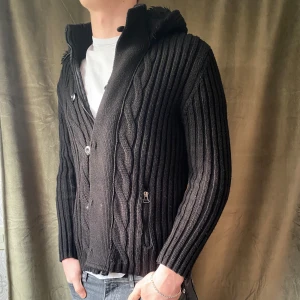 Cardigan med fodrad luva - Snygg svart stickad kofta med dragkedja och knappar framtill. Den har en mysig huva med foder och ribbade detaljer. Perfekt för kyliga dagar. Luvan är avtagbar. Det är storlek L men sitter mer som M. Vid minsta fråga eller fundering hör av er🤝