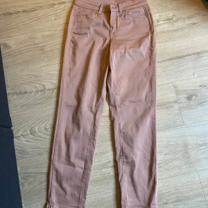 Beige chinos - Snygga beige chinos med normal passform och hög midja. Perfekta för en stilren look. De har en klassisk design med knappar och dragkedja framtill.