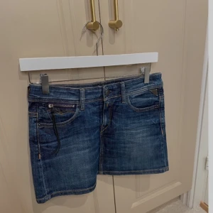 Blå jeansskjol från Replay - Snygga blå jeanskjol från Replay med klassisk femficksdesign och knappgylf. Perfekta för en avslappnad stil. Märkesdetaljer på insidan av linningen.