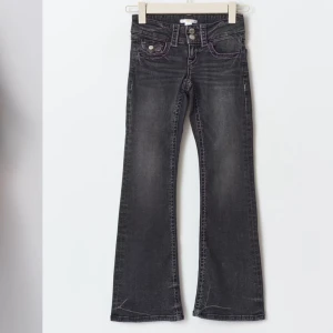 Mörkgrå lowaist bootcut jeans - Snygga mörkgrå bootcut jeans med låg midja och dubbla knappar. Perfekta för en trendig look med en skön passform. De har klassiska femfickor och en lätt tvättad effekt för extra stil. Jeansen är köpta för 299kr på gina tricots barnavdelning. De är i storlek 170 men skulle säga att de är som xs/s. Jeansen är i mycket fint skick 