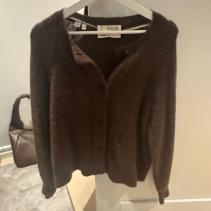 Brun kofta från Selected - Mysig brun kofta från Selected med knappar framtill. Perfekt för kyligare dagar och enkel att matcha med olika outfits.