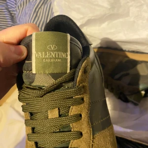 Valentino Garavani sneakers i camouflage - Snygga Valentino Garavani sneakers med ett coolt camouflagemönster. Skorna har snörning och är tillverkade i en kombination av mocka och skinn. Perfekta för en trendig look.