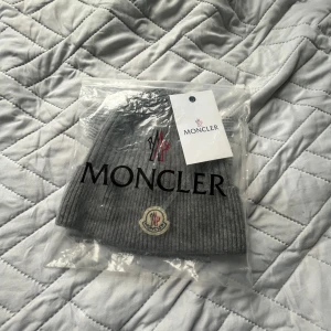 Grå ribbad mössa från Moncler - Snygg grå ribbad mössa från Moncler med broderad logotyp framtill. Perfekt för kyliga dagar och ger en stilren look. Mössan är tillverkad i ett mjukt och bekvämt material. Köptes i vintras men används försiktigt och inga skador🤗🤗10/10skick👌🏻