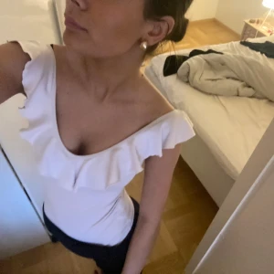 Vit volang body  - Säljer en stilren vit offshoulder topp med volangdetaljer. 