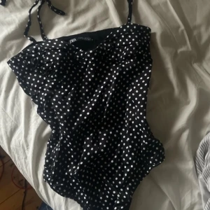 Svart prickig body från Zara - Snygg svart body från Zara med vita prickar och justerbara axelband. Perfekt fest topp! Dragkedjan är tyvärr sönder som jag visar på bilden men det är inte svårt att fixa!