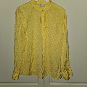 Second Female ljusgul blus nytt - Oanvänd Snygg ljusgul blus med prickar och rosett i halsen. Blusen har volanger vid halsen och vid ärmsluten.  Nypris 1299 kr  Märke second female