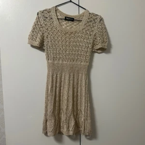 Champagne färgad stickad klänning  - Charmig champagne stickad klänning med korta ärmar och ett vackert hålmönster som glittrar. Perfekt för en avslappnad stil med sin mjuka och bekväma passform. Finns i marinblå och röd! Passar storlek XXS-S.