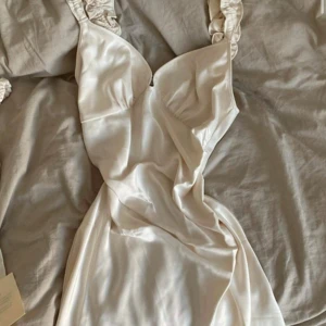 Adoore Natal klänning helt ny! - Elegant vit klänning med detaljer på axelbanden. Klänningen har en v-ringad design och är perfekt för vintern som sommarens festligheter. Helt ny med lappar kvar därav oanvänd, endast provad! Slutsåld online, verkligen ett kap!