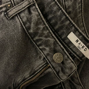 GråSvarta raka jeans från NA-KD - Snygga gråsvarta jeans från NA-KD med en klassisk design. De har en dragkedja och knapp framtill samt fickor både fram och bak. Perfekta för en stilren look. Raka och medelhög midja. Passar storlek 42-44