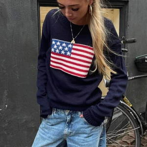 Mörkblå stickad tröja med amerikansk flagga - Säljer en skitsnygg mörkblå stickad tröja med en stor amerikansk flagga på framsidan. Tröjan har långa ärmar och en rund halsringning. Använd ett fåtal gånger. Köpt för 460kr. Första bild tagen från hemsidan