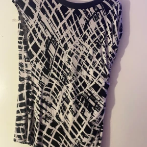 Svartvit mönstrad topp från Lindex - Snygg svartvit topp från Lindex med ett abstrakt rutmönster. Toppen har en rund halsringning och är ärmlös, vilket gör den perfekt för varmare dagar eller lager-på-lager-stil.