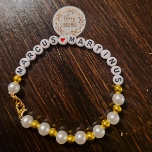 Marcus & Martinus armband hemmagjort  - Charmigt armband med vita och guldiga pärlor samt bokstäver som bildar 'MARCUS MARTINUS'. Perfekt som en personlig accessoar eller present.