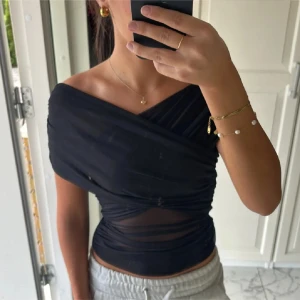 Svart offshoulder topp - Snygg svart offshoulder topp med omlott-design och transparenta detaljer. Perfekt för en stilren look. Endast använd en gång.💗