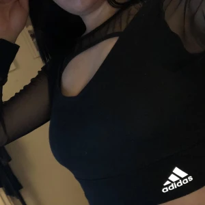 Svart croppad topp från Adidas - Snygg svart croppad topp från Adidas med transparenta meshdetaljer vid hals och ärmar. 