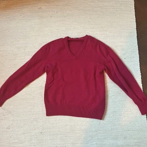 Mörk rosa  tröja från Barrie - Säljer en stilren vinröd tröja från Barrie med v-ringning. Tröjan har långa ärmar och är perfekt för kyligare dagar. Tillverkad i Skottland, vilket garanterar hög kvalitet.