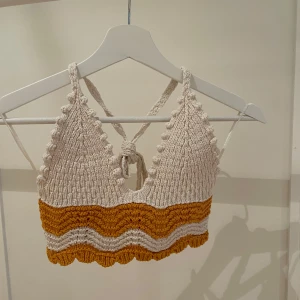 Stickad topp från Zara - Säljer en stickad topp från Zara i beige och orange med ett vågigt mönster. Toppen är ärmlös och har knytning i ryggen. Perfekt för sommardagar!