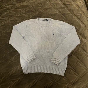 Stickad tröja från Polo Ralph Lauren - Säljer en ljusblå stickad tröja från Polo Ralph Lauren. Tröjan har en broderad logotyp på bröstet och ribbade muddar vid ärmslut och nederkant. Perfekt för kyligare dagar!