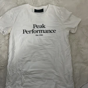 Vit t-shirt från Peak Performance - Säljer en klassisk vit t-shirt från Peak Performance med tryck 'Est. 1986' på framsidan. T-shirten har en normal passform och korta ärmar, perfekt för en avslappnad stil. Passar tjejer lika bra som killar👍