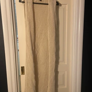 Beige stickad klänning från Lindex - Säljer en beige stickad klänning från Lindex. Den är ärmlös och har ett luftigt, nätliknande mönster. Perfekt för lager-på-lager-stil eller som ett somrigt plagg.