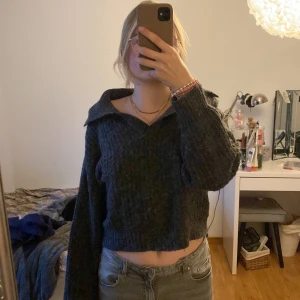 Mörkgrå stickad tröja - Säljer en mysig mörkgrå stickad tröja med krage och croppad passform. Perfekt för kyliga dagar och ger en stilren look. Tröjan har långa ärmar och är enkel att matcha med olika outfits.