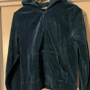 Petrol färgad velourjacka med dragkedja - Säljer en snygg petrol färgad velourjacka med dragkedja och huva. Jackan har långa ärmar och praktiska fickor framtill. Perfekt för en avslappnad stil.