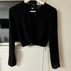 Svart blus från Divided - Snygg svart blus från Divided med långärmad design. Blusen har en enkel och stilren look med rund hals och elastisk nederkant. Perfekt för en chic och minimalistisk stil.