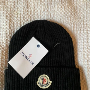 Svart mössa från Moncler - Snygg svart mössa från Moncler med det klassiska broderade logotypmärket framtill. Perfekt för att hålla värmen under kyliga dagar.