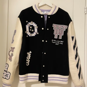 College jacka från Off-White - Snygg svart och vit bomberjacka från Off-White med coola broderade detaljer och tryck. Jackan har långa ärmar i kontrasterande färg och knappar framtill. Perfekt för dig som vill sticka ut med stil!