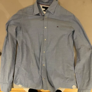 Blå skjorta från Tommy Hilfiger - Snygg blå skjorta från Tommy Hilfiger i slim fit med stretch. Skjortan har långa ärmar och klassiska knappar framtill. Perfekt för en stilren look. Riktigt grisch. Sparsamt använd, har bara använt den på jul afton o midsommarafton. 