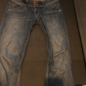 Blå jeans från Replay - Säljer ett par snygga blå jeans från Replay. De har en klassisk femficksdesign med knappar fram och coola detaljer på bakfickorna. Perfekta för vardagsbruk och kan enkelt matchas med en t-shirt eller skjorta.