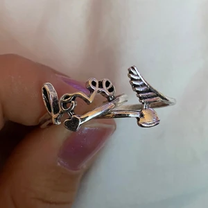 Ringar  - Två silverringar, ena där det står ”Love” och den andra med en fjäder och ett hjärta. Båda är ungefär 2cm i diameter. 