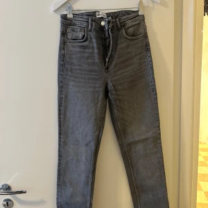 Grå jeans från Zara - Säljer ett par snygga grå jeans från Zara i storlek 38. De har en klassisk design med dragkedja och knapp framtill. Perfekta för både vardag och fest!